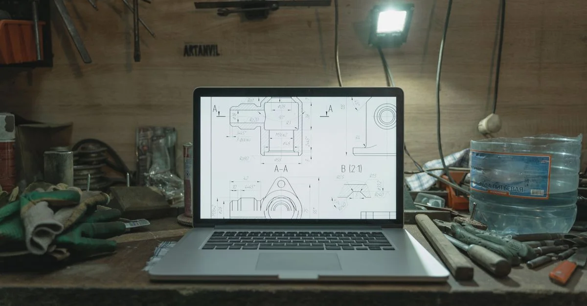Un ordinateur portable affichant des plans sur un établi en désordre dans un atelier.